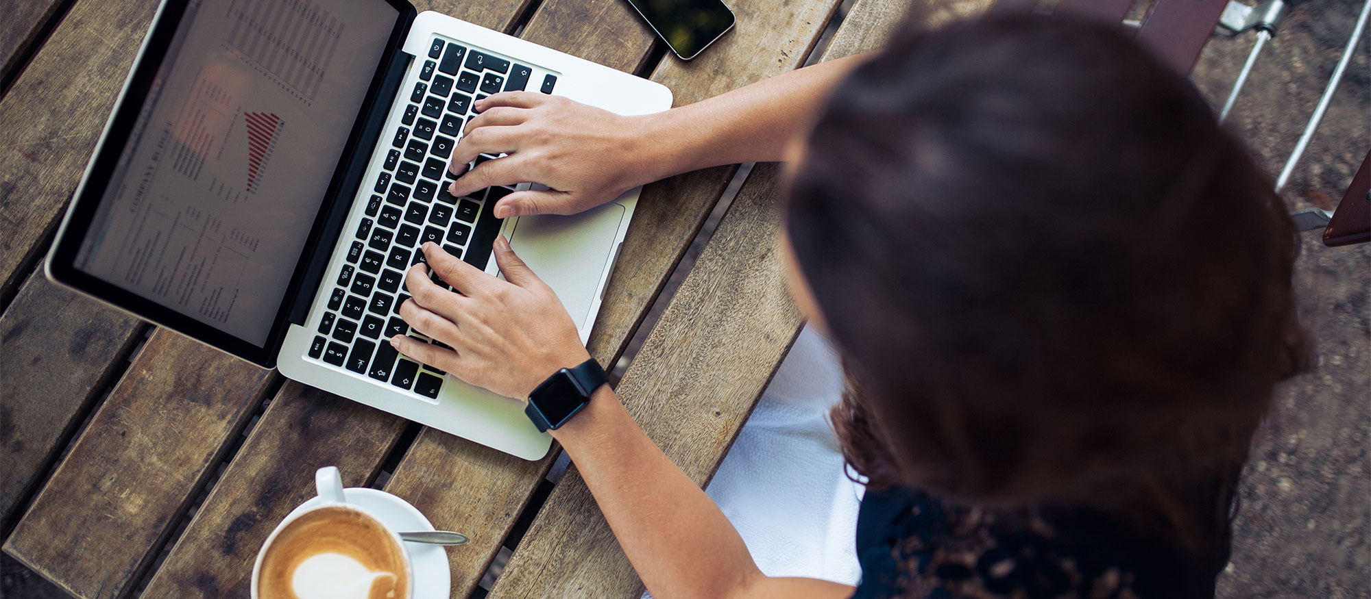 Kvinna sitter ute med en kaffe latte vid ett bord och jobbar på sin laptop
