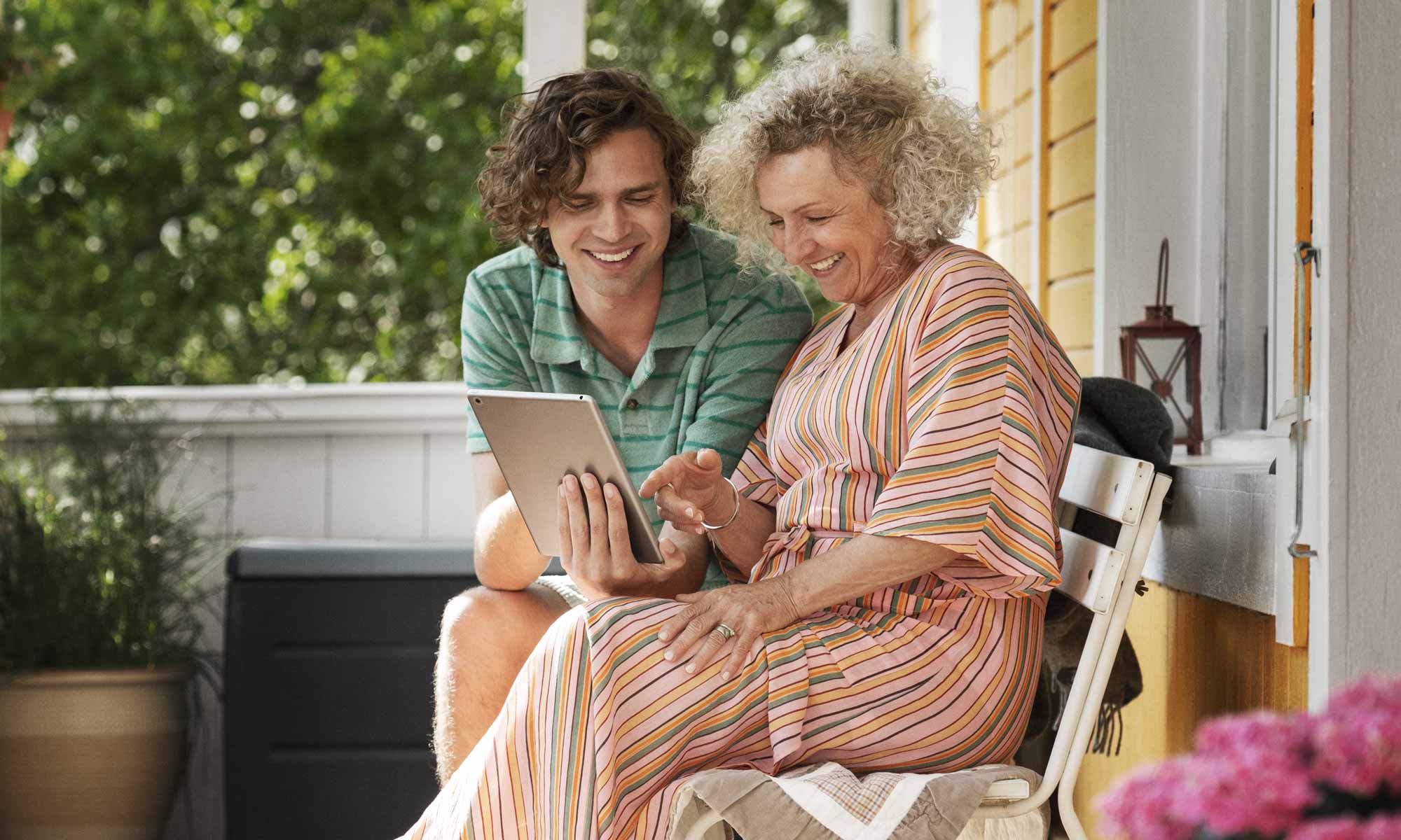 Mamma med sin äldre son sitter ute på verandan och tittar på en iPad
